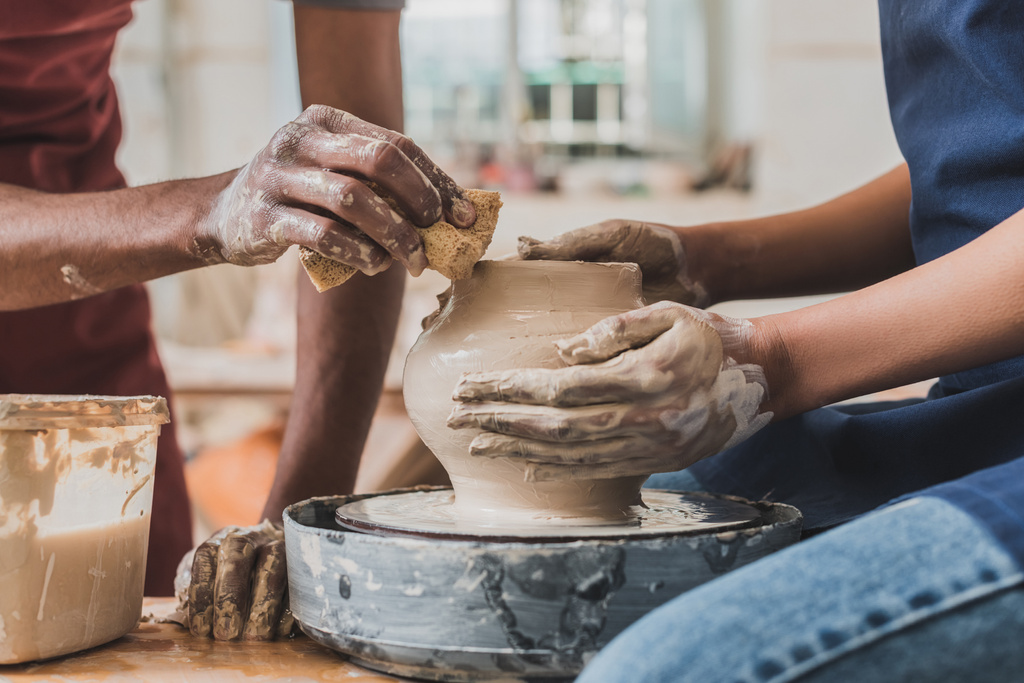 partial view of young african american couple in aprons sculpting pot on wheel with wet sponge in pottery - Fotoğraf, Görsel