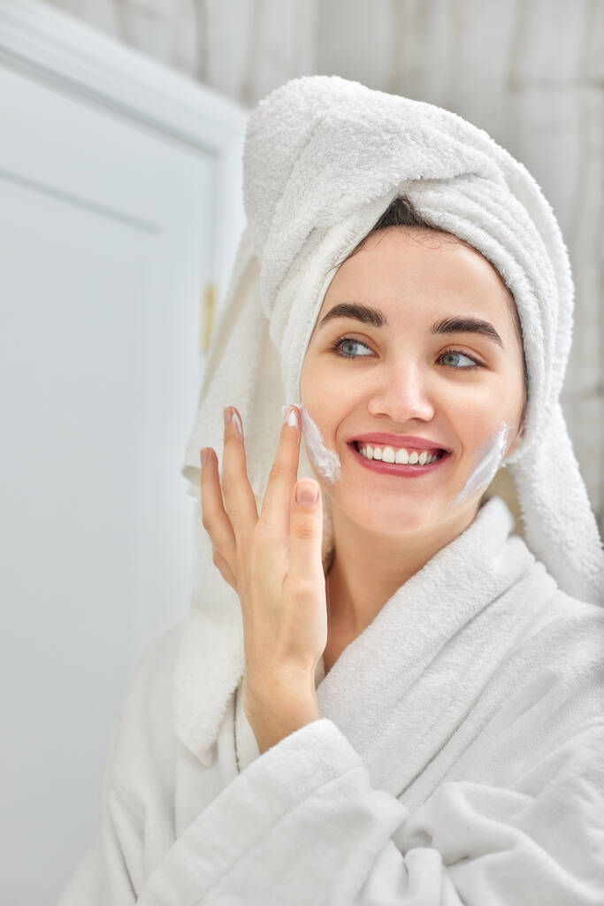 nő fehér fürdőköpenyben alkalmazása alkalmazni arckrém - Fotó, kép