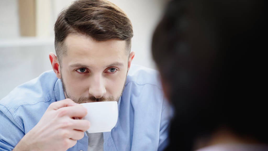Adam kahve içiyor ve bulanık kız arkadaşına bakıyor.  - Fotoğraf, Görsel