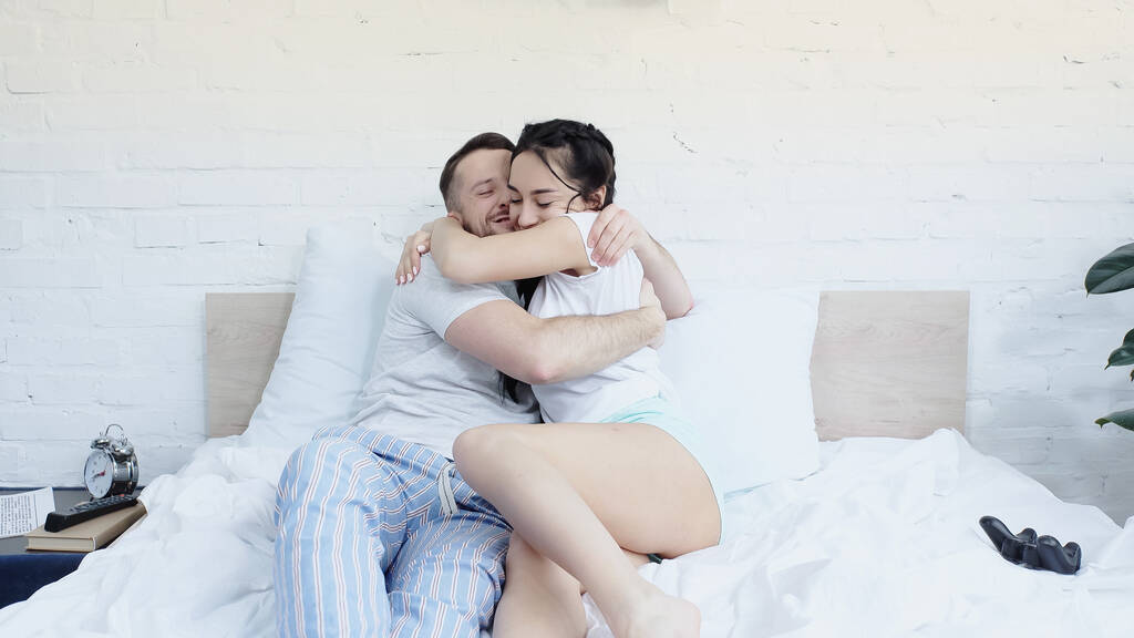 KYIV, UKRAINE - 2021年6月17日:明るいカップルがベッドの上でジョイスティックの近くに抱擁 - 写真・画像