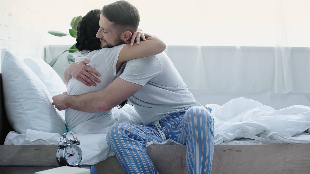 bebaarde man zitten op bed en knuffelen vriendin  - Foto, afbeelding