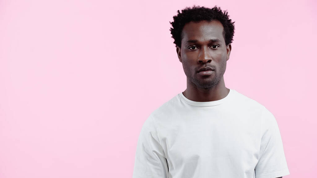 seriózní africký Američan v bílém tričku při pohledu na kameru izolované na růžové - Fotografie, Obrázek