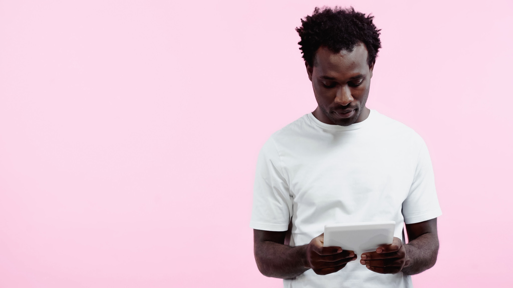 ピンクで区切られたデジタルタブレットを使用して白いTシャツのアフリカ系アメリカ人男性を巻き - 写真・画像