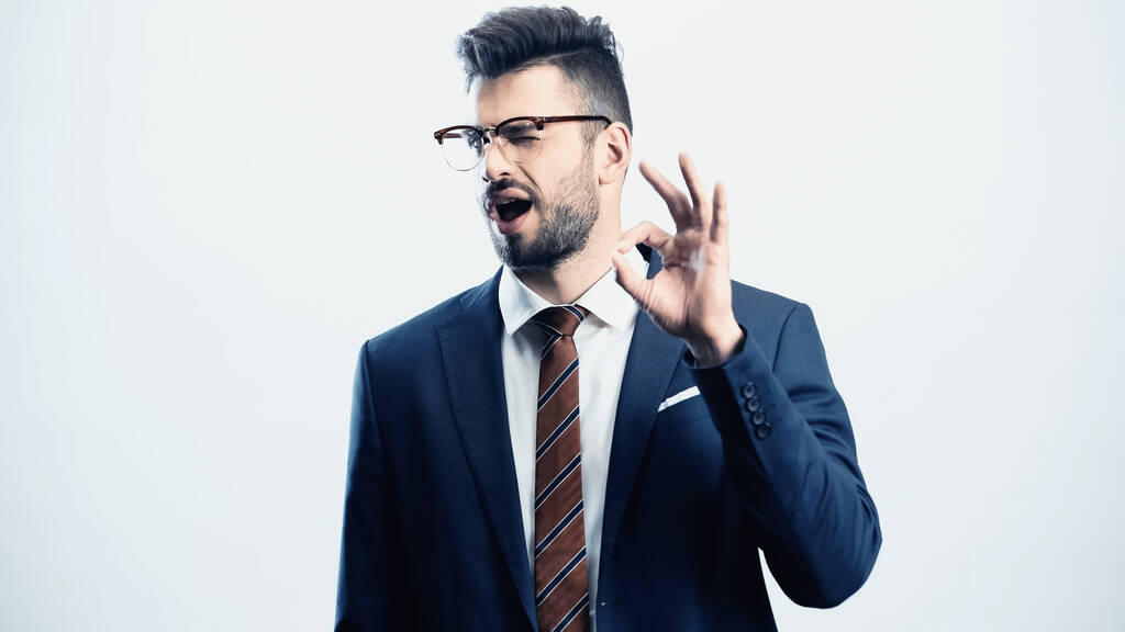 hombre de negocios positivo mostrando buen gesto mientras guiña un ojo a la cámara aislada en blanco - Foto, imagen