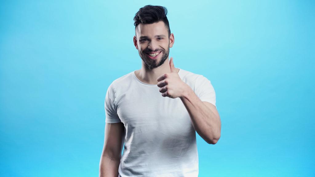 smiling man looking at camera and showing thumb up isolated on blue - Photo, Image