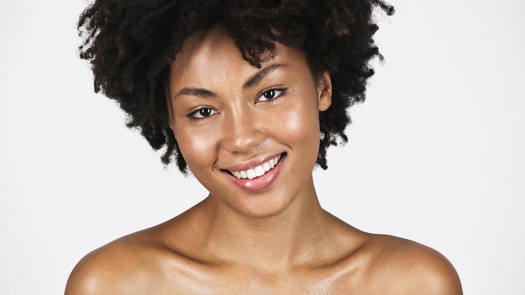 Młoda Afroamerykanka z czystą skórą i nagimi ramionami uśmiechnięta na szaro  - Zdjęcie, obraz