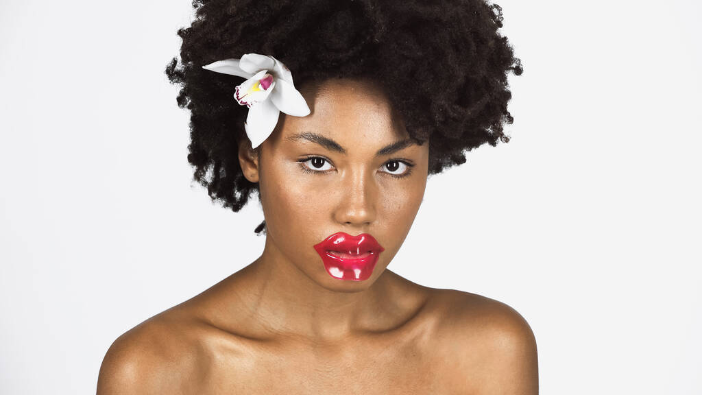 Joven mujer afroamericana con parche en los labios y flor en el pelo aislado en gris  - Foto, imagen