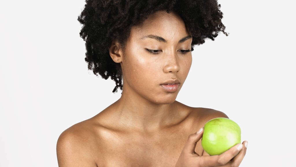 Afroamerykanka z idealną skórą trzymająca zielone jabłko odizolowane na szaro  - Zdjęcie, obraz