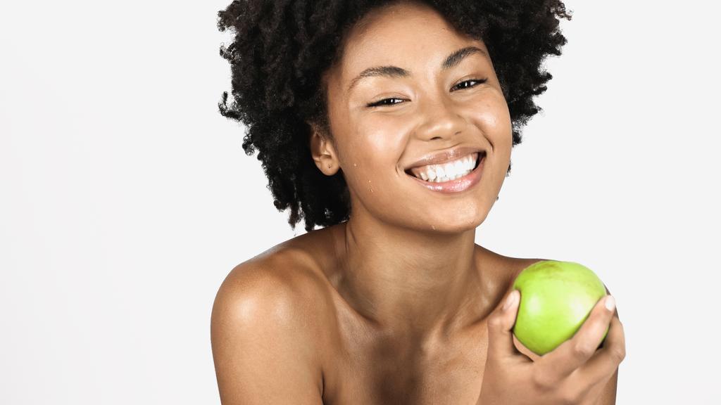 Pozitív afro-amerikai nő csupasz vállakkal, lédús zöld almát tartva elszigetelve a szürkén.  - Fotó, kép