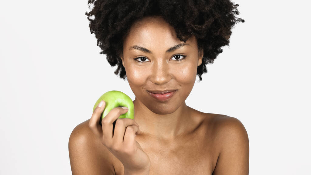 Усміхнена афроамериканка з чистою шкірою, що тримає ціле яблуко ізольовано на сірому
  - Фото, зображення