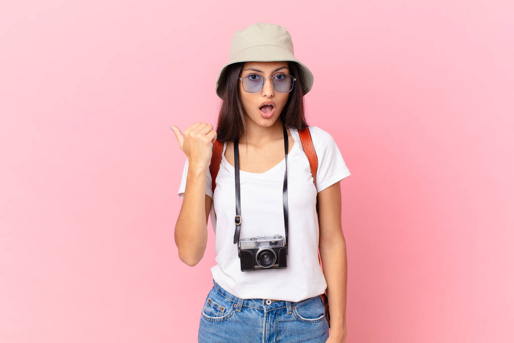 pretty hispanic tourist looking astonished in disbelief with a photo camera and a hat - Foto, afbeelding