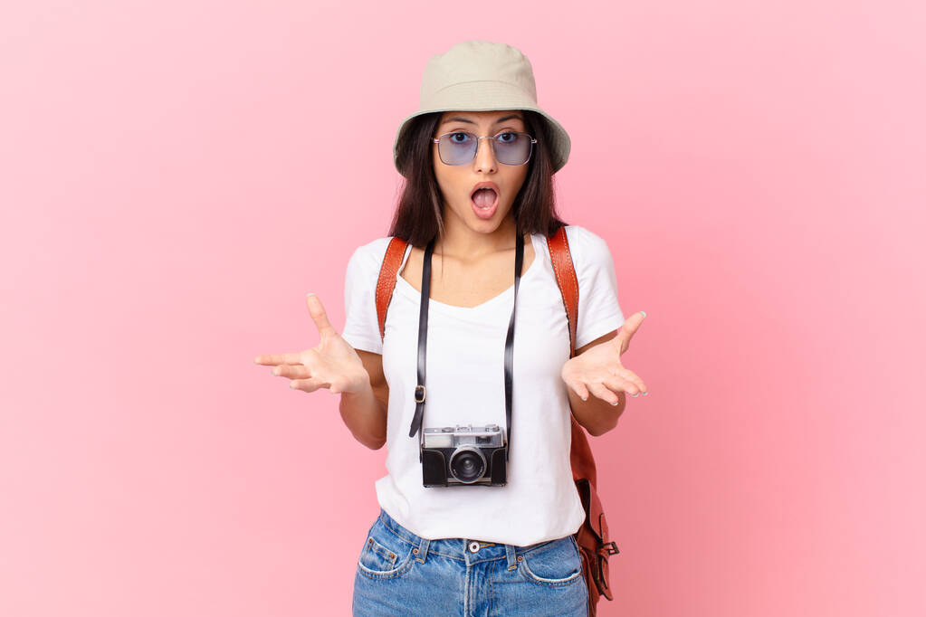 pretty hispanic tourist feeling extremely shocked and surprised with a photo camera and a hat - Fotoğraf, Görsel