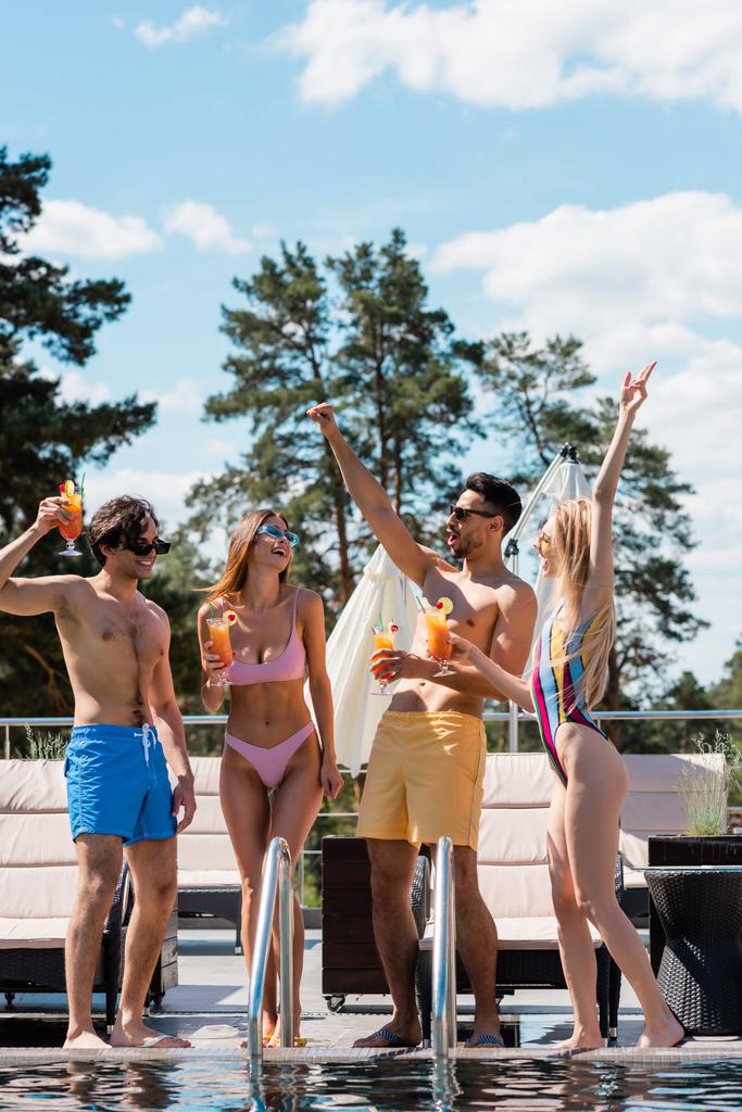 Веселі багатоетнічні люди з коктейлями жестикулюють біля басейну
  - Фото, зображення