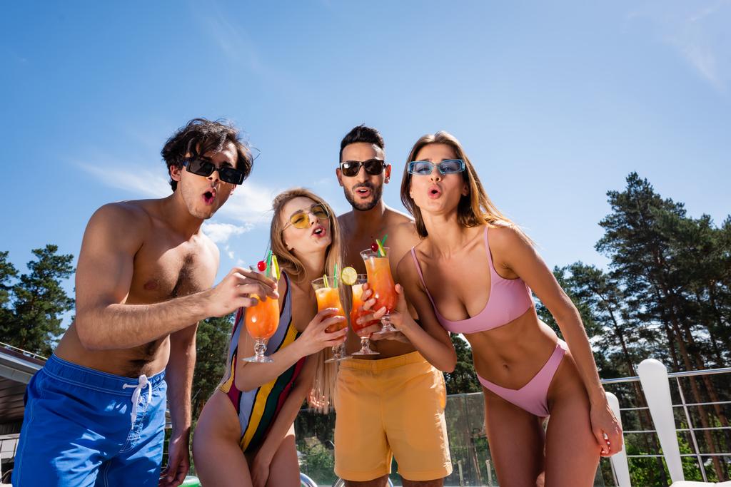 Low angle view of excited multiethnic friends holding cocktails at resort  - Photo, Image