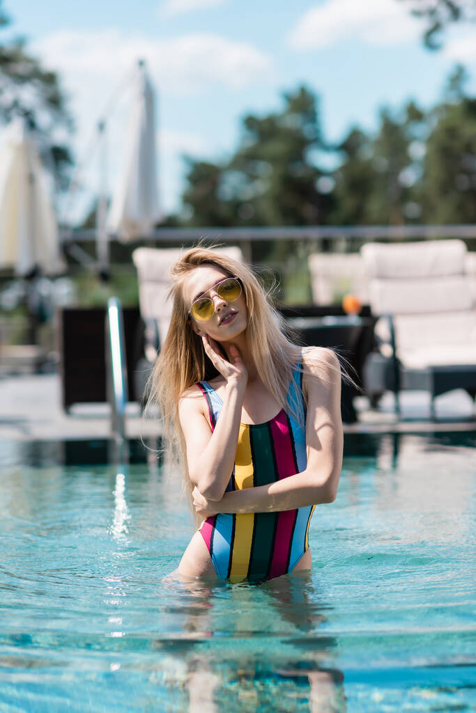 mooie vrouw in gestreepte badpak staan in zwembad buiten  - Foto, afbeelding