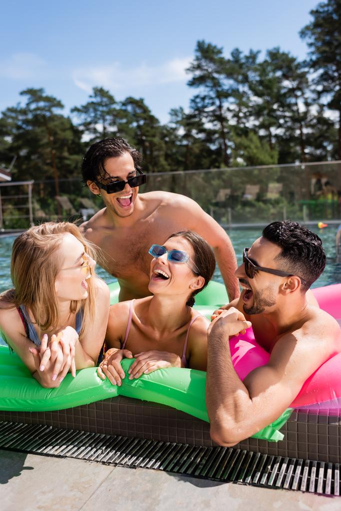 веселі багатоетнічні друзі сміються над надувним матрацом у басейні
 - Фото, зображення