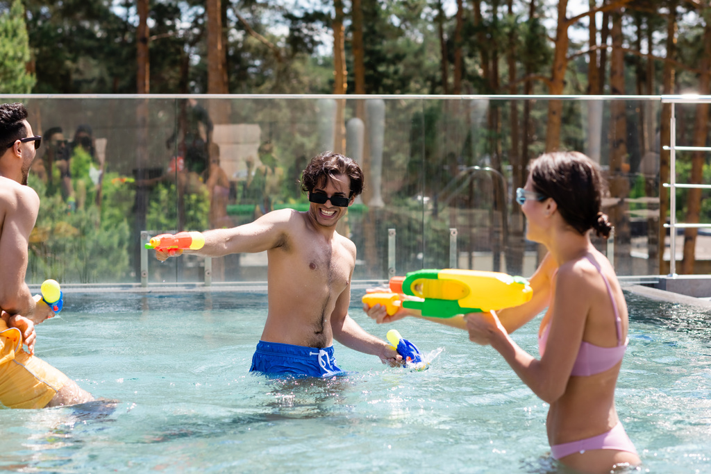 amigos interracial emocionados jugando juego de batalla de agua en la piscina - Foto, imagen