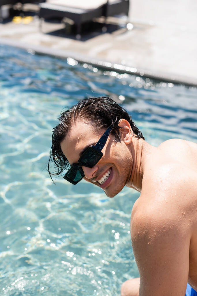 fiatal félmeztelen férfi napszemüvegben mosolygós medence mellett - Fotó, kép