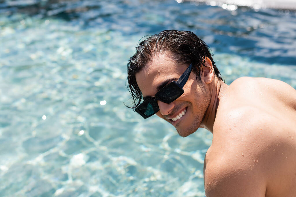 Junger Mann mit Sonnenbrille lächelt am Pool - Foto, Bild