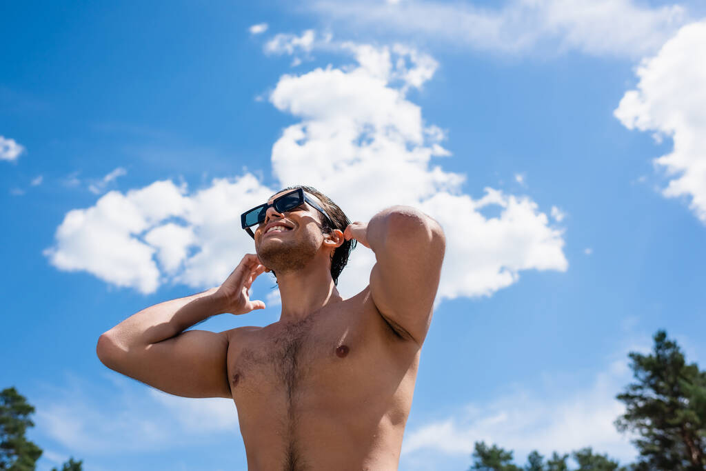 низький кут зору молодого без сорочки чоловіка на фоні блакитного неба на відкритому повітрі
 - Фото, зображення