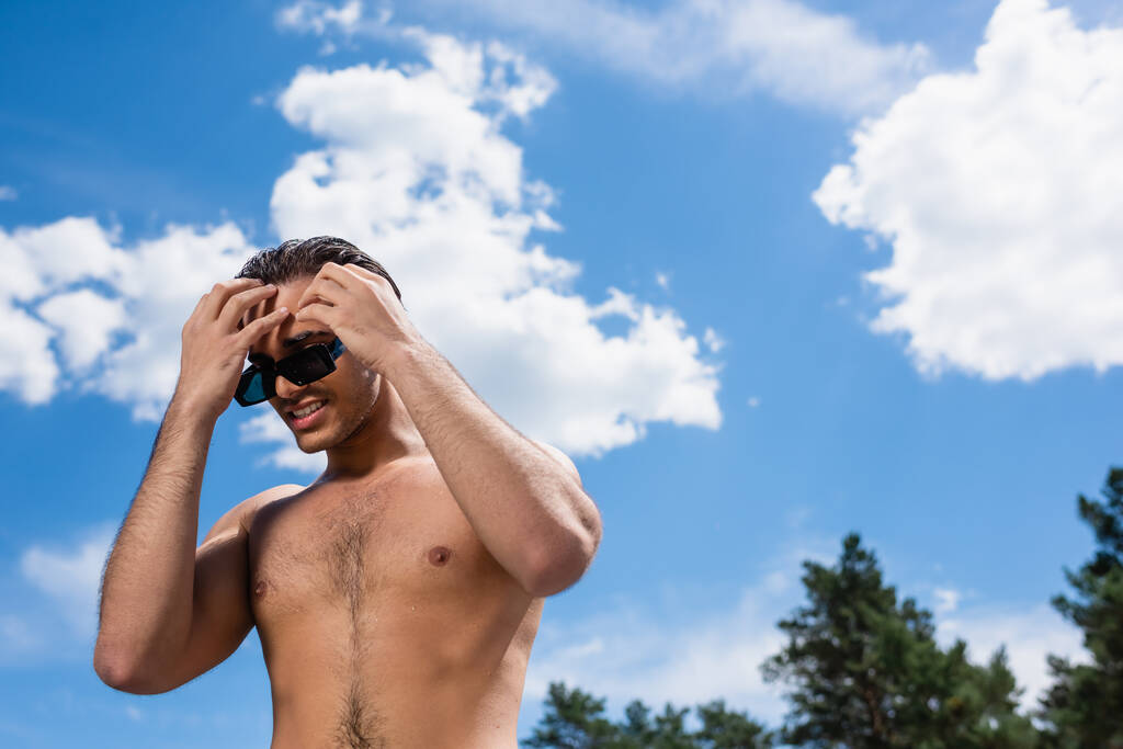 низкий угол зрения на человека без рубашки касаясь волос на открытом воздухе - Фото, изображение