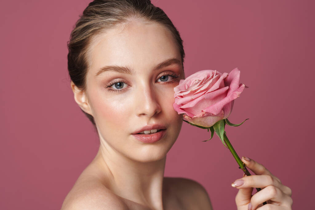 Κοντινό πορτρέτο ομορφιάς μιας ελκυστικής νεαρής γυναίκας που ποζάρει με ένα τριαντάφυλλο απομονωμένο σε ροζ φόντο - Φωτογραφία, εικόνα