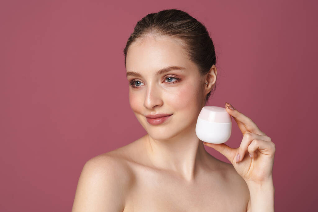 Close up retrato de beleza de uma jovem atraente mostrando frasco de creme facial isolado sobre fundo rosa - Foto, Imagem