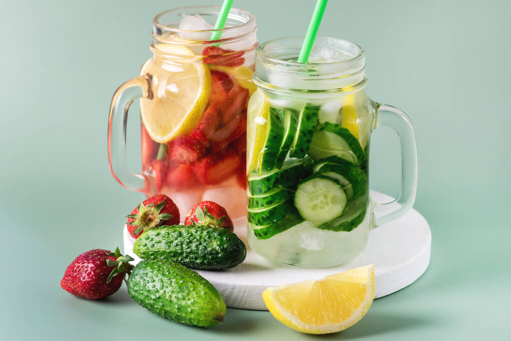 різноманітні холодні літні напої у скляних посудинах наповнювали детоксикаційну воду огірком лимоном і полуницею здоровим напоєм зеленим фоном. - Фото, зображення