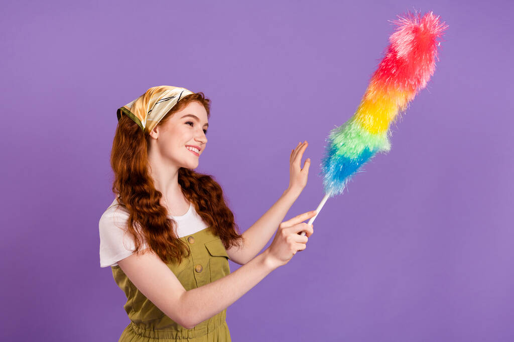 Портрет привлекательной веселой девушки, вытирающей пыль бытовые обязанности изолированы на фиолетовом фиолетовом фоне - Фото, изображение