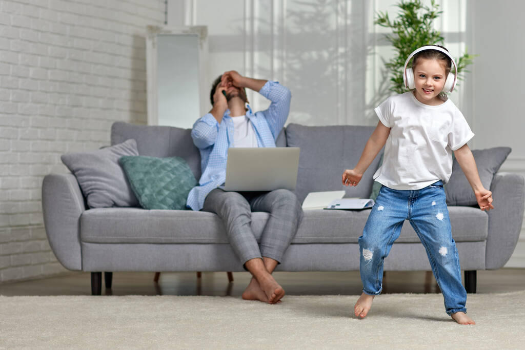 niño bailando y ocupado papá trabajando con el ordenador portátil en casa - Foto, imagen