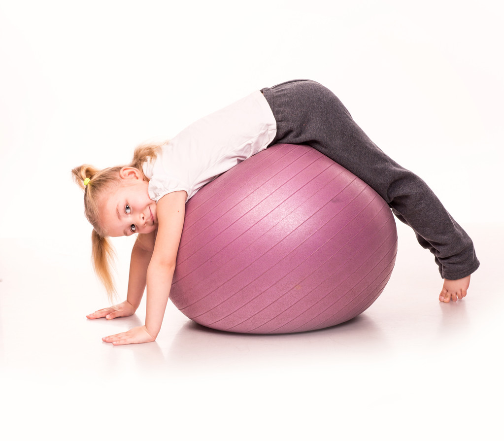 Menina esportiva em uma bola de ajuste isolado sobre branco
 - Foto, Imagem