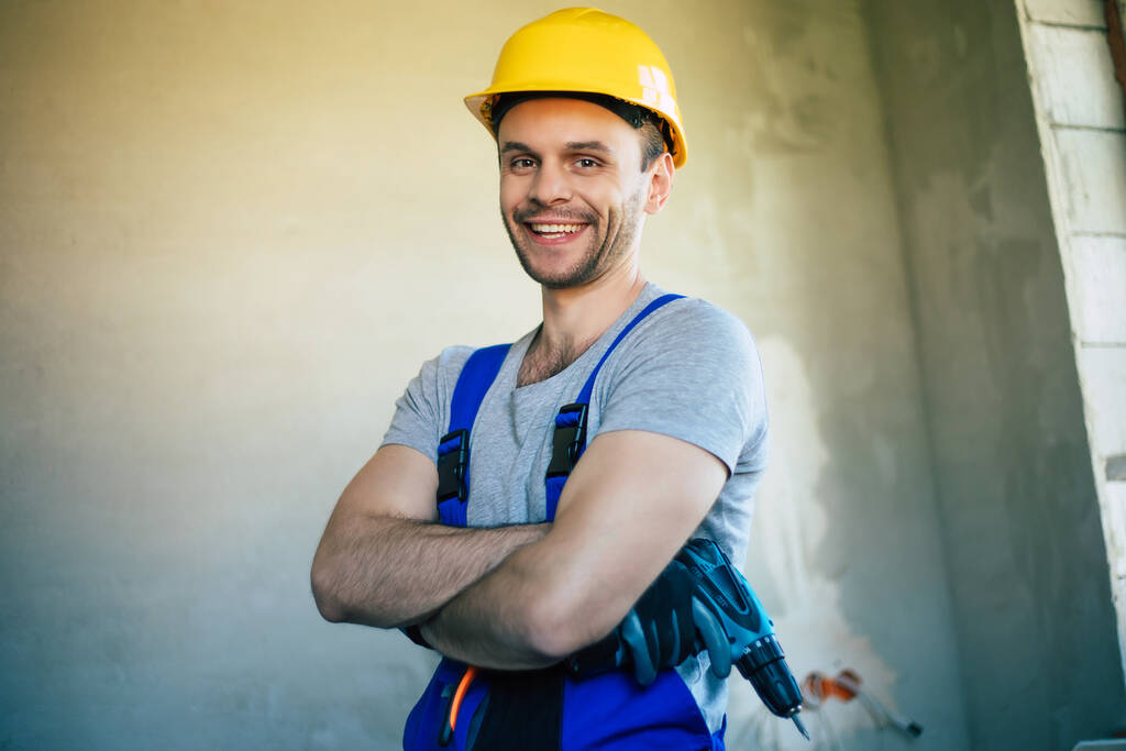 Junge Hausreparaturmännchen oder Arbeiter, die mit Hausrenovierung beschäftigt sind, halten Baugeräte in der Hand, tragen im Neubau lässige Arbeitskleidung - Foto, Bild