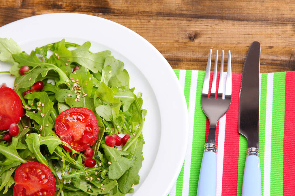 Salada verde feita com arugula, tomates e gergelim na placa, no fundo de madeira
 - Foto, Imagem