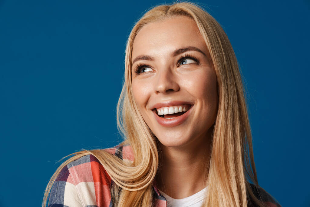 Blonde young happy woman smiling and looking aside isolated over blue background - Photo, Image
