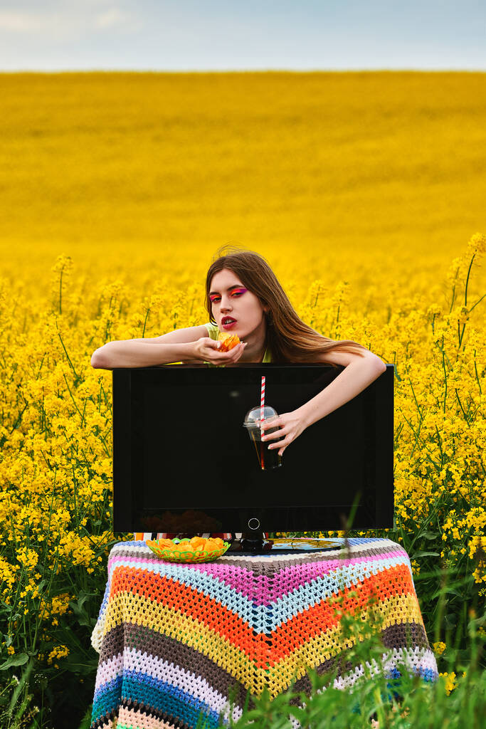νεαρή κοπέλα τρώει μάρκες και πίνει ένα ποτό στο πεδίο με τηλεόραση. έννοια διακοπών. δημιουργικό - Φωτογραφία, εικόνα
