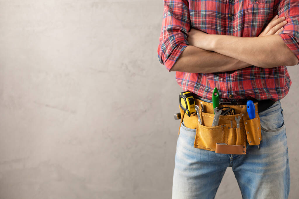 Hombre trabajador y cinturón de herramientas cerca de la pared. Mano masculina y herramientas de construcción. Concepto de renovación o reparación - Foto, Imagen