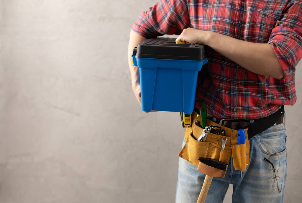 Hombre trabajador sosteniendo caja de herramientas y cinturón de herramientas cerca de la pared. Mano masculina y herramientas de construcción. Concepto de renovación o reparación - Foto, imagen