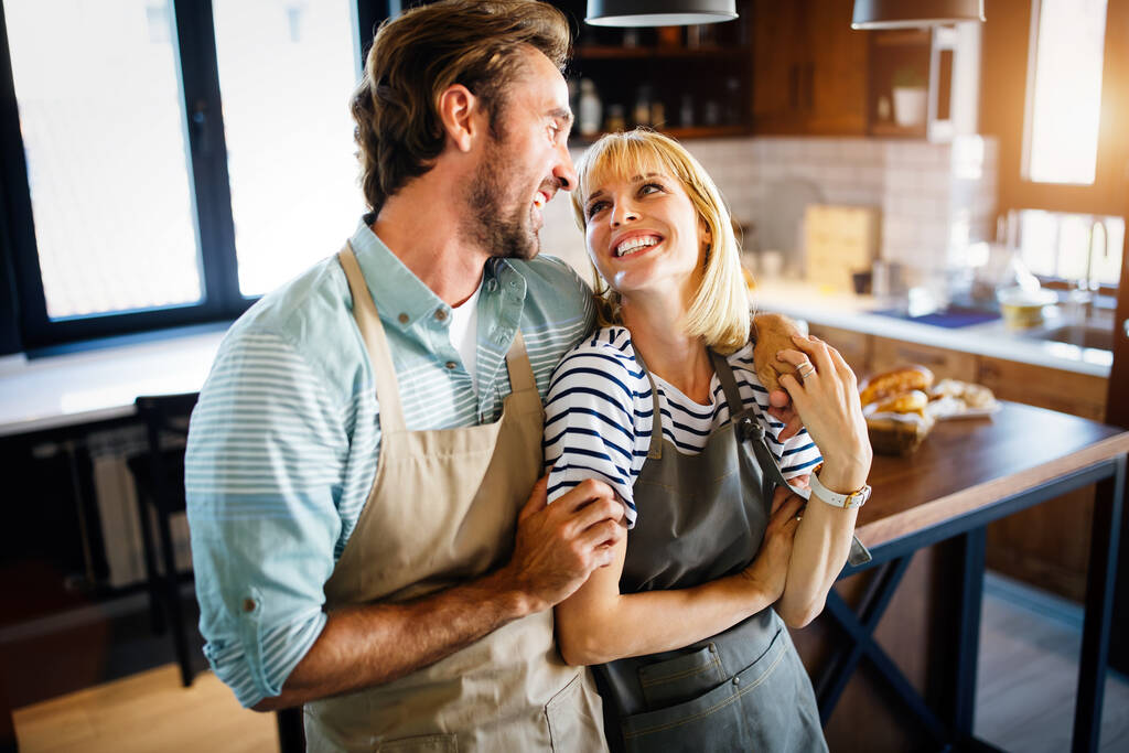 Hermosa joven pareja encantadora está hablando y sonriendo mientras cocina comida saludable en la cocina en casa - Foto, Imagen