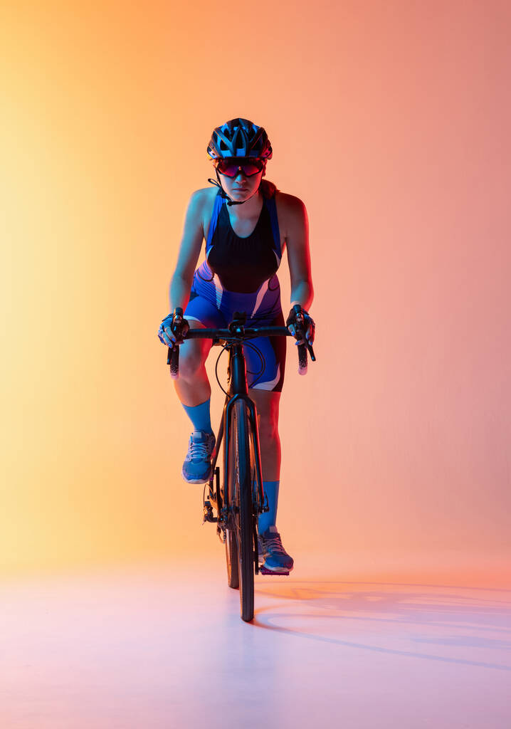 Vista frontale. Ciclista donna in sella a una bicicletta isolata sullo sfondo al neon - Foto, immagini