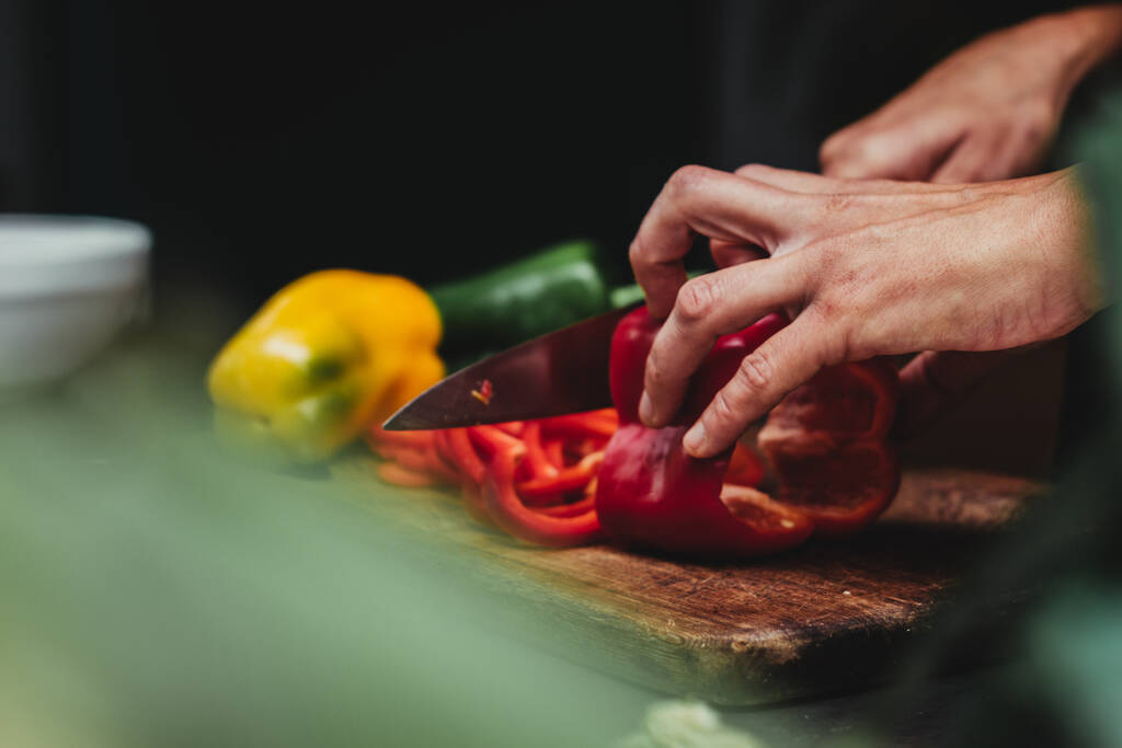 A person cutting colorful bell pepper on a wooden cutting board - Photo, Image