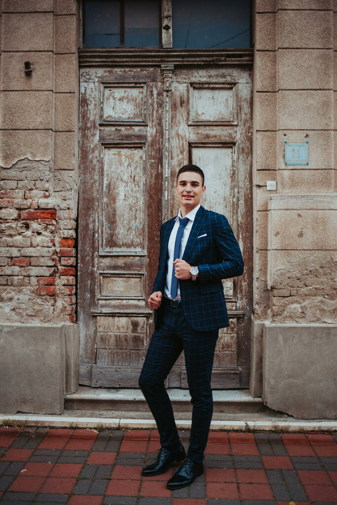 Молодой кавказский бизнесмен в костюме и галстуке позирует перед дверью - Фото, изображение