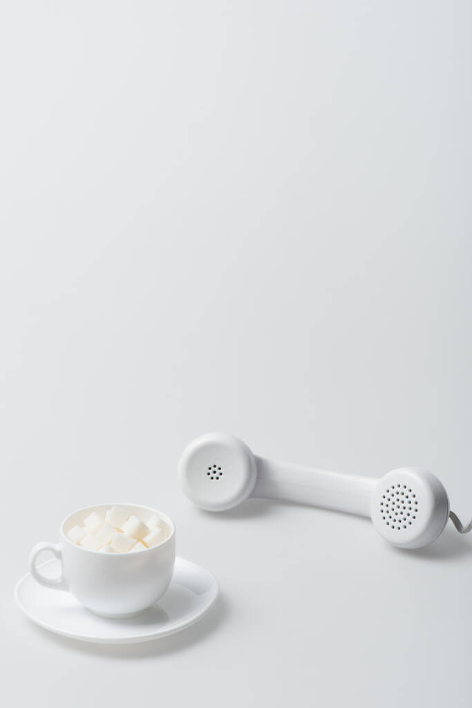 cubos de azúcar en taza con platillo cerca del teléfono retro en blanco - Foto, imagen