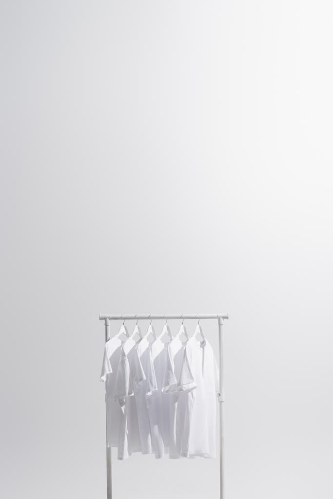 λευκά t-shirts κρέμονται σε σχάρα ρούχα απομονώνονται σε γκρι  - Φωτογραφία, εικόνα