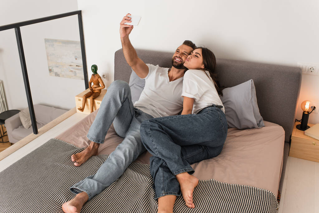 Mutlu çift yatakta cep telefonuyla selfie çekiyor.  - Fotoğraf, Görsel