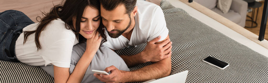 Couple utilisant un smartphone près d'un ordinateur portable flou sur le lit, bannière  - Photo, image