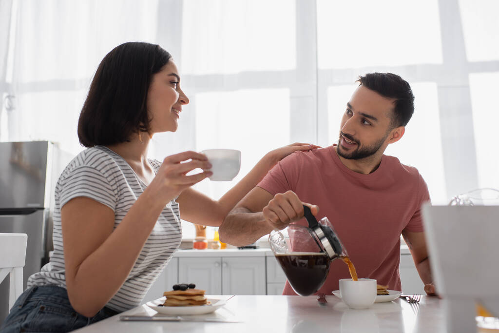 sorridente giovane donna con coppa commovente fidanzato con caffettiera in cucina - Foto, immagini