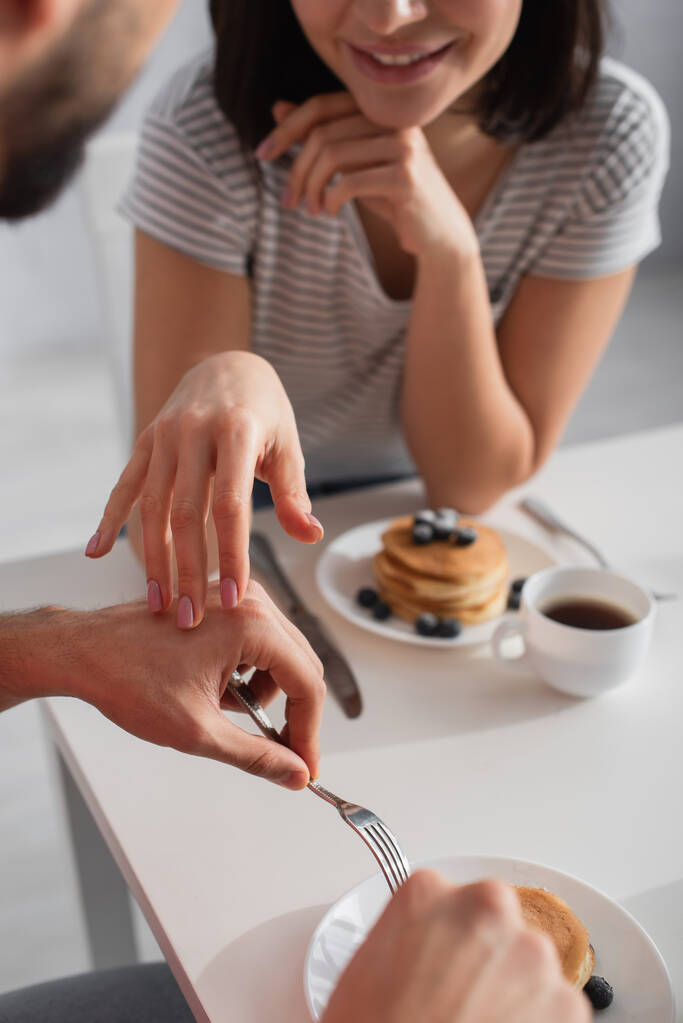 částečný pohled mladé ženy dotýkající se ruky přítele jíst snídani v kuchyni - Fotografie, Obrázek