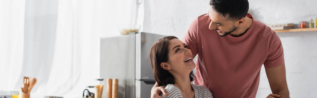 glimlachende jonge man knuffelen vriendin in keuken, banner - Foto, afbeelding