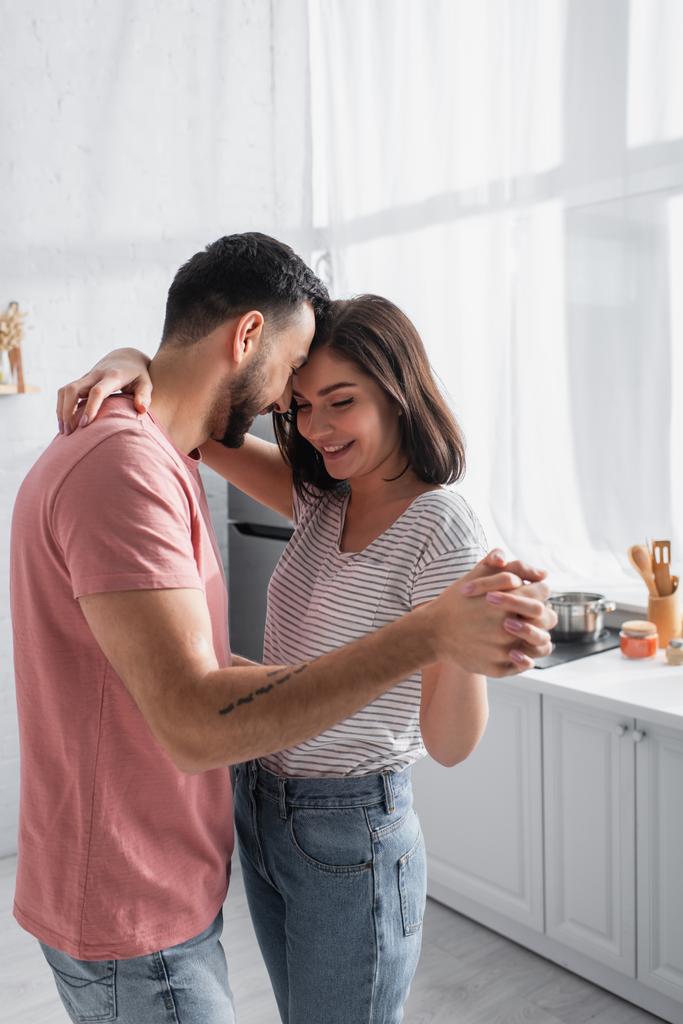 sorrindo jovem casal em camisetas e jeans dançando na cozinha - Foto, Imagem