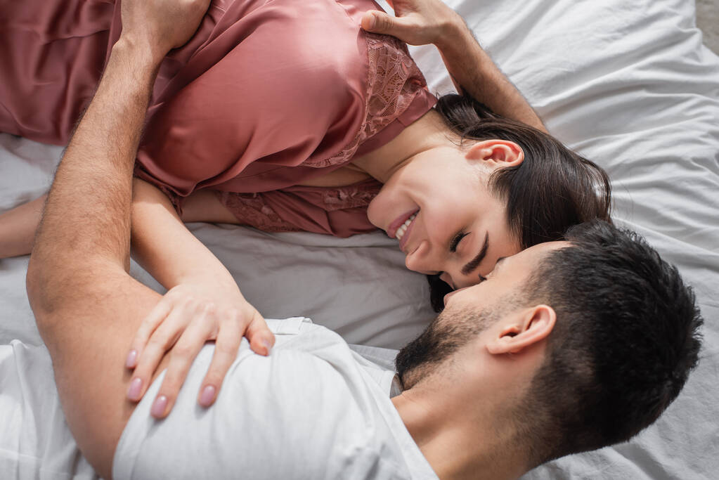 ylhäältä näkymä nuori mies makaa sängyllä valkoiset liinavaatteet ja varovasti halaamalla tyttöystävä makuuhuoneessa - Valokuva, kuva
